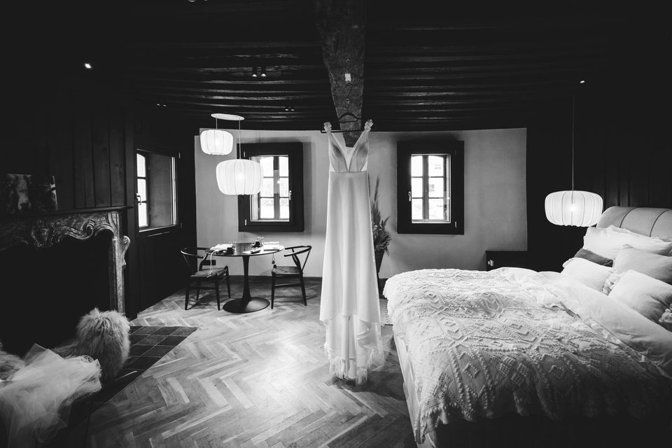 Das Brautkleid hängt in einem dunklen Zimmer mit Fischgrätparkett und hellen Papierleuchten